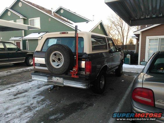 1992 Ford Bronco parked under a carport, spare tire mounted on rear, Hi-Lift jack attached