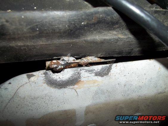 Close-up of a rusted metal bracket attached to a pipe, with a black hose above