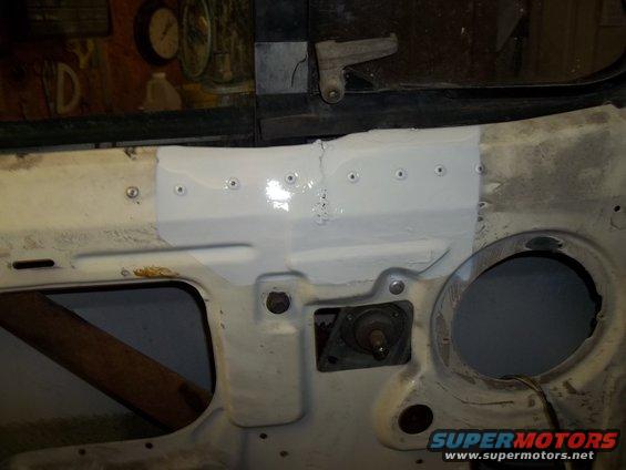 Vehicle firewall with patched section, showing rivets and a circular opening