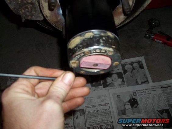 Close-up of a vehicle hub assembly with a hand holding a tool, resting on newspapers