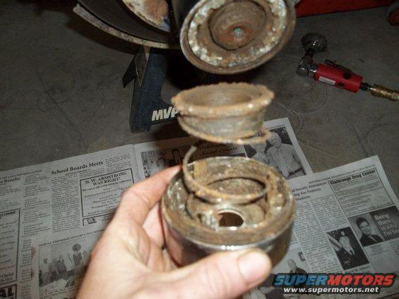 hand holding rusty spring and cap assembly, newspaper and jack stand in background