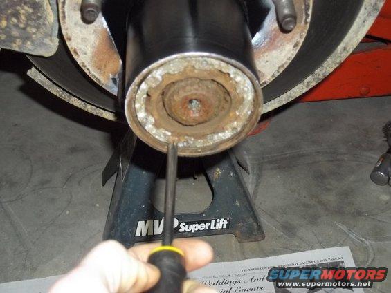 Close-up of a rusty wheel hub assembly on a jack stand, with a screwdriver being used