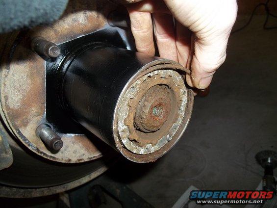 Close-up of a person's hands working on a rusty vehicle hub assembly, possibly replacing a part