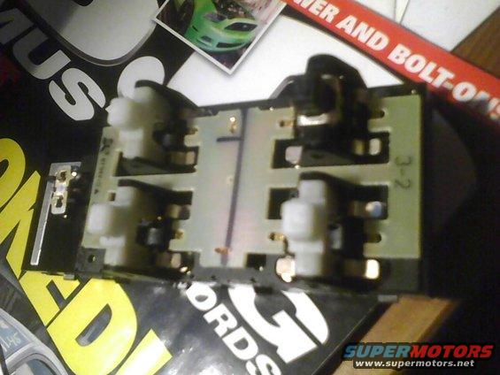 Electrical component with white and black connectors on a circuit board, with text and a small image in the background