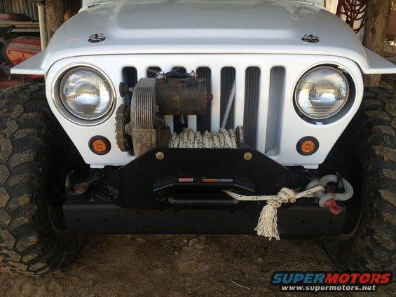 Front of a white Jeep TJ with a winch mounted on the bumper. It has large off-road tires