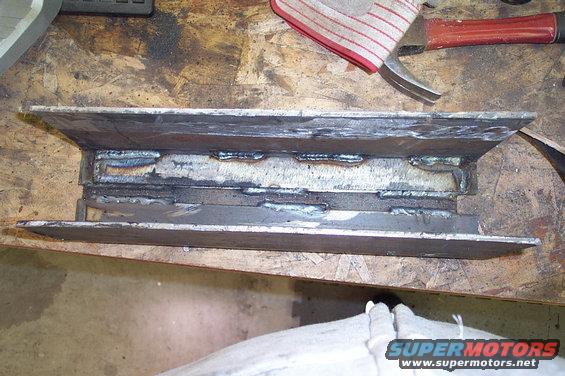 Welded metal part on workbench with hammer and glove