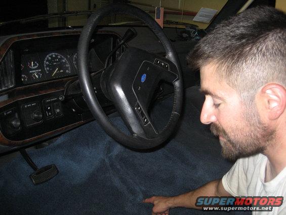 1989 Ford Bronco interior with blue carpet, wood trim dashboard, and steering wheel. A man is pointing at the carpet
