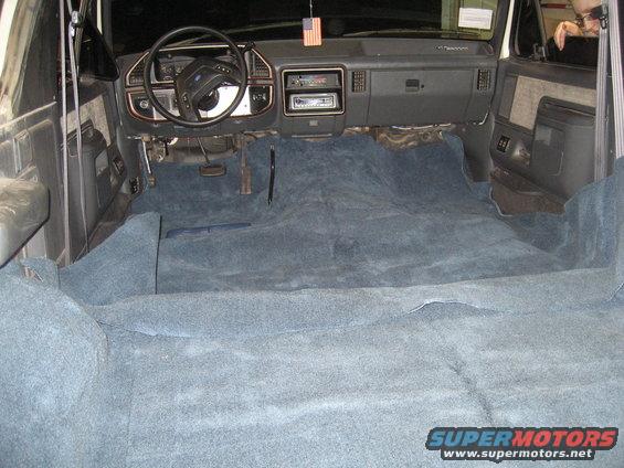 Interior of a 1989 Ford Bronco with blue carpet installed. Shows dashboard, steering wheel, and front seats