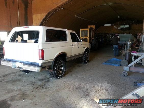 White Ford Bronco parked in garage with yellow loader behind it