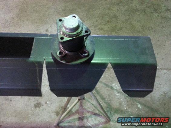Close-up of a metal automotive part with a four-bolt flange mounted on a dark metal structure