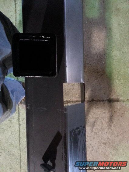 Black trailer hitch receiver with a square opening, attached to a metal frame. A blue cloth is visible to the left