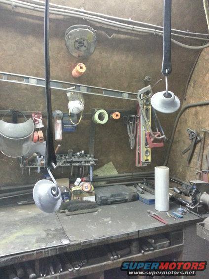 Workbench with tools hanging on wall and on surface. A metal part hangs from a hook