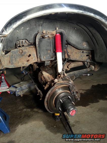 Front suspension and wheel assembly with red shock absorber, brake rotor, and hub. Vehicle is on jack stands