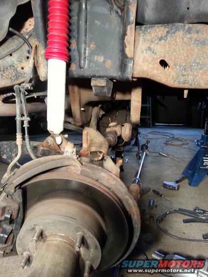 Front suspension and brake assembly with red-booted shock absorber, rusty frame, and tools on the floor