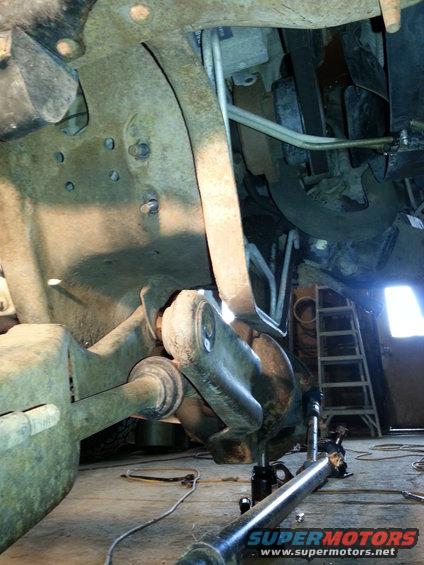 Rusty vehicle suspension parts with hydraulic lines and a ladder in the background