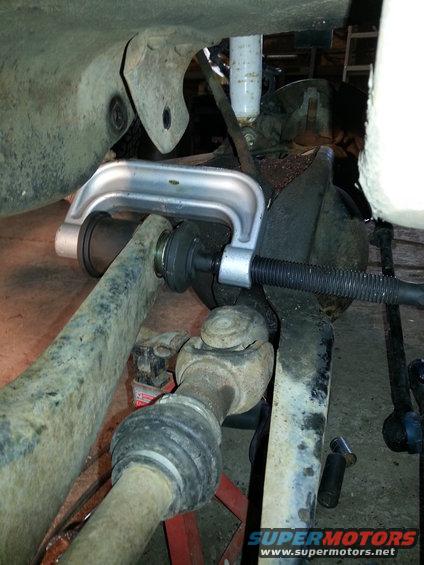Ball joint press tool compressing a suspension component, with driveshaft visible