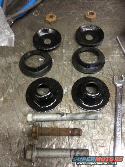 Four black spring isolators and two nuts with three bolts on a metal surface