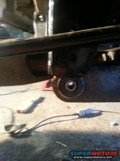 Close-up of a vehicle's suspension bushing and mounting bracket, with a red jack stand visible in the background