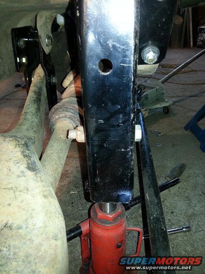 Vehicle frame section supported by red hydraulic jack, with suspension parts visible