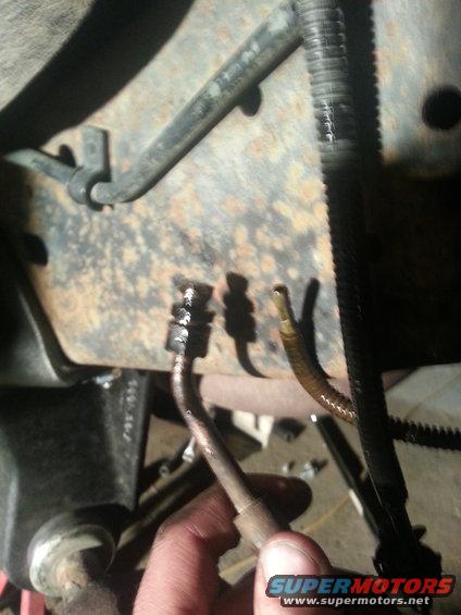 Close-up of rusted vehicle frame with brake lines and a hand holding a metal tube