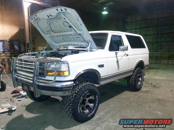 White Ford Bronco, hood open, in a garage. Lifted suspension and aftermarket grille guard visible