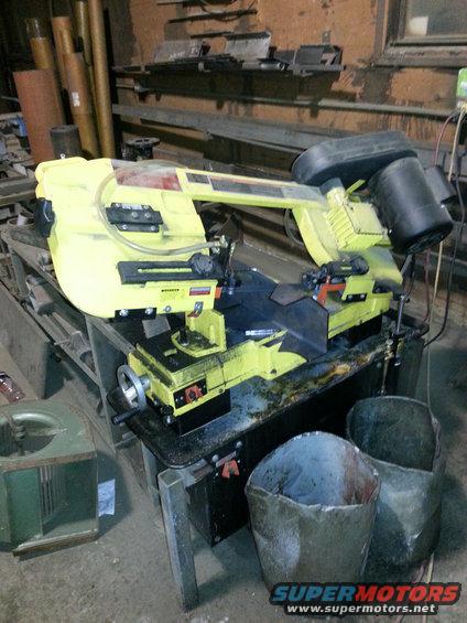 Yellow and black band saw on a workbench in a workshop, with metal scraps in buckets