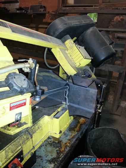 Yellow metal cutting bandsaw with black motor and guards, cutting metal