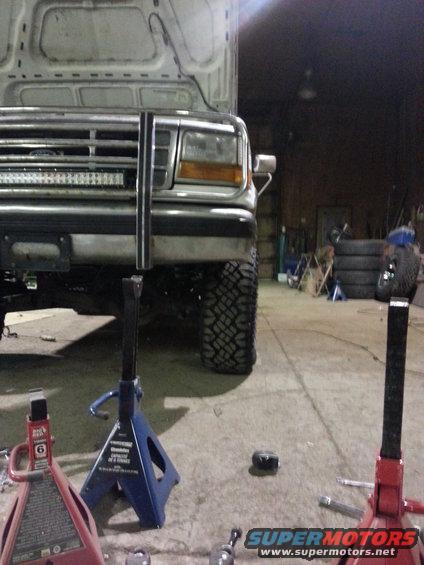 Front of a lifted Ford truck with a light bar, on jack stands. Tires are large and knobby