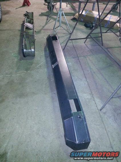 Two aftermarket bumpers, one with a silver finish and one black, on a concrete floor
