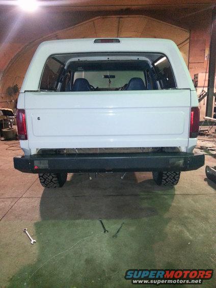 Rear view of a white SUV with a black bumper and blue interior seats visible