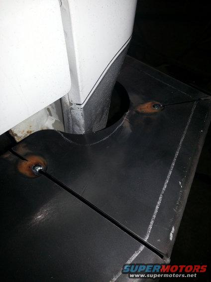 White vehicle panel edge with black trim above black metal fabrication with a hole and weld