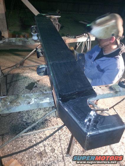 Black aftermarket bumper on sawhorses, being worked on by a welder
