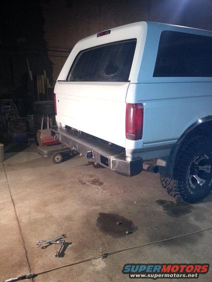 White SUV, possibly a Bronco, with a new metal rear bumper installed. Tools are on the floor
