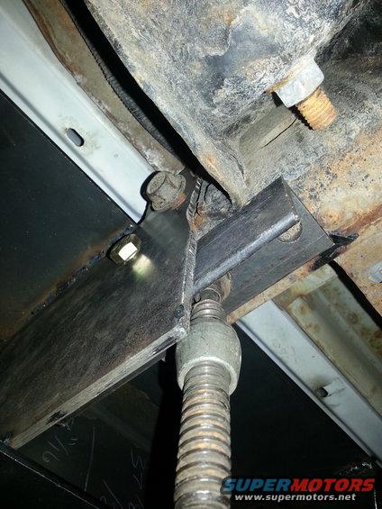 Undercarriage of a vehicle with rust and a metal bracket attached to a screw jack