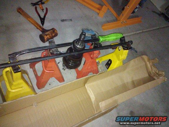 Car parts including a transmission and tools on jack stands