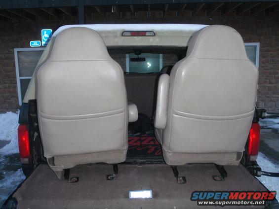 Two tan bucket seats are loaded into the cargo area of a vehicle. Snow is visible outside