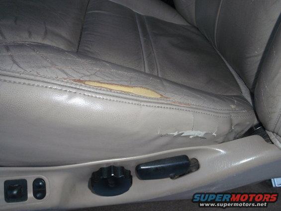 Close-up of worn tan leather car seat with tear on the side cushion and cracked leather. Seat adjustment controls visible