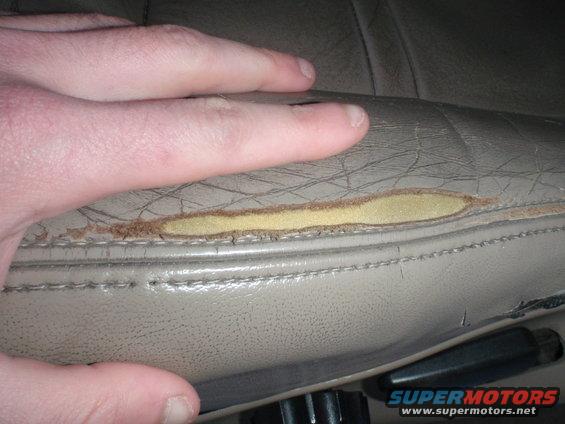 hand on torn leather car seat, showing exposed foam