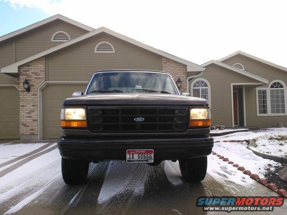 Front view of a dark-colored Ford F-150 truck parked in a driveway with snow on the ground. The grille has a prominent Ford emblem