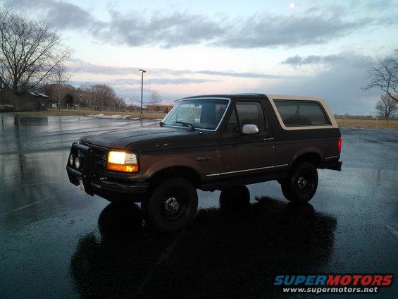 Dark brown and tan Ford Bronco parked on a wet asphalt lot