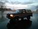 1992 Ford Bronco - A two-tone Ford Bronco sits in a wet parking lot under a cloudy sky.