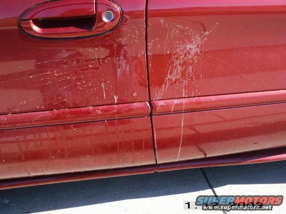 Red car door and fender with bird droppings and scratches