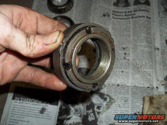 Hand holding a used wheel bearing lock nut with visible threads and locking tabs