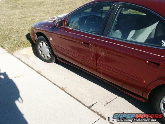 maroon sedan parked on a concrete driveway next to grass. The car is a four-door with a white pinstripe along the side