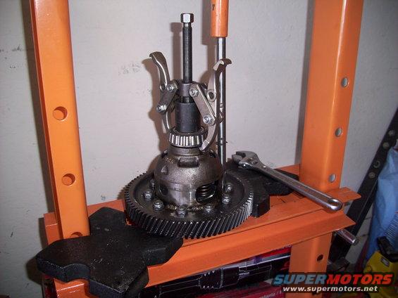Differential gear assembly being worked on with a puller tool and wrench on an orange press