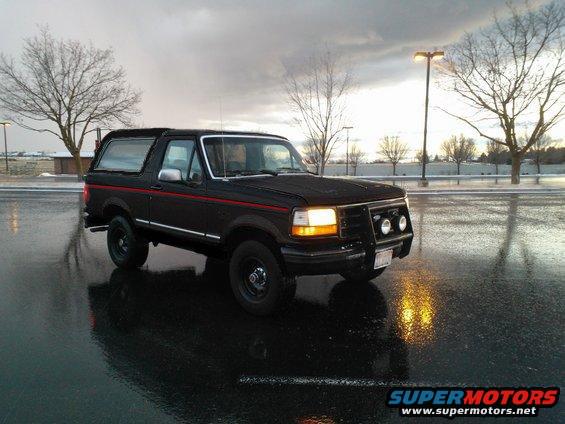 Black Ford Bronco parked on wet asphalt, overcast sky