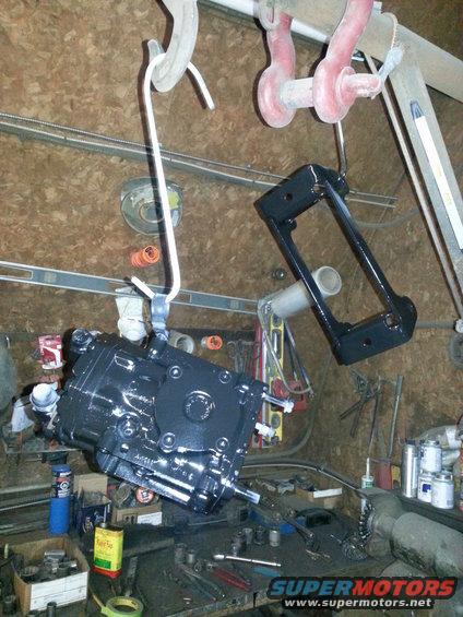 Black painted automotive part hanging from a hook in a workshop, with tools and other parts on a workbench below