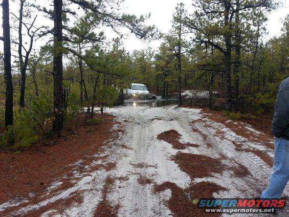 1987 Toyota 4Runner driving through mud on a dirt road in a wooded area