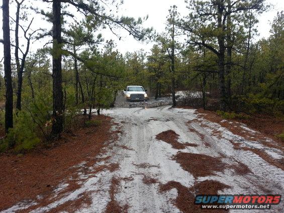 White pickup truck driving on a sandy, wooded dirt road