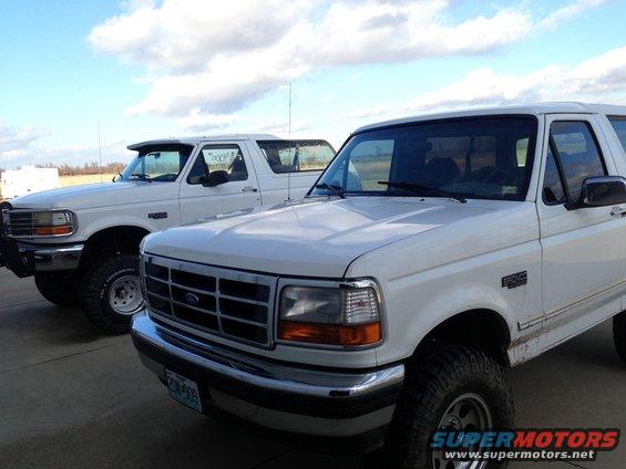 Two white Ford Broncos parked side-by-side, front Bronco in foreground, showing grille and headlights